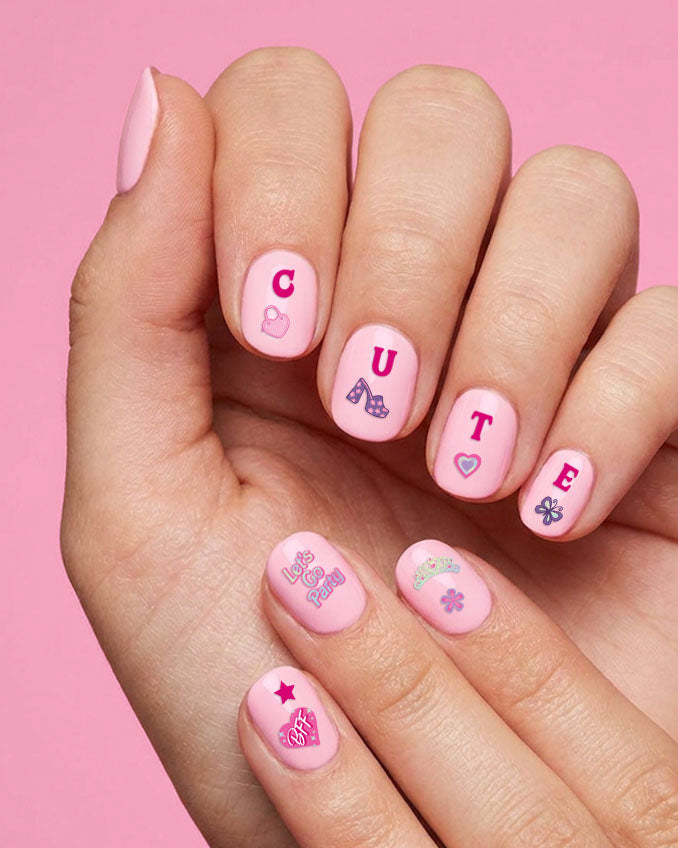 Hand with pink nails spelling CUTE in nail stickers with hearts, bows, and a star