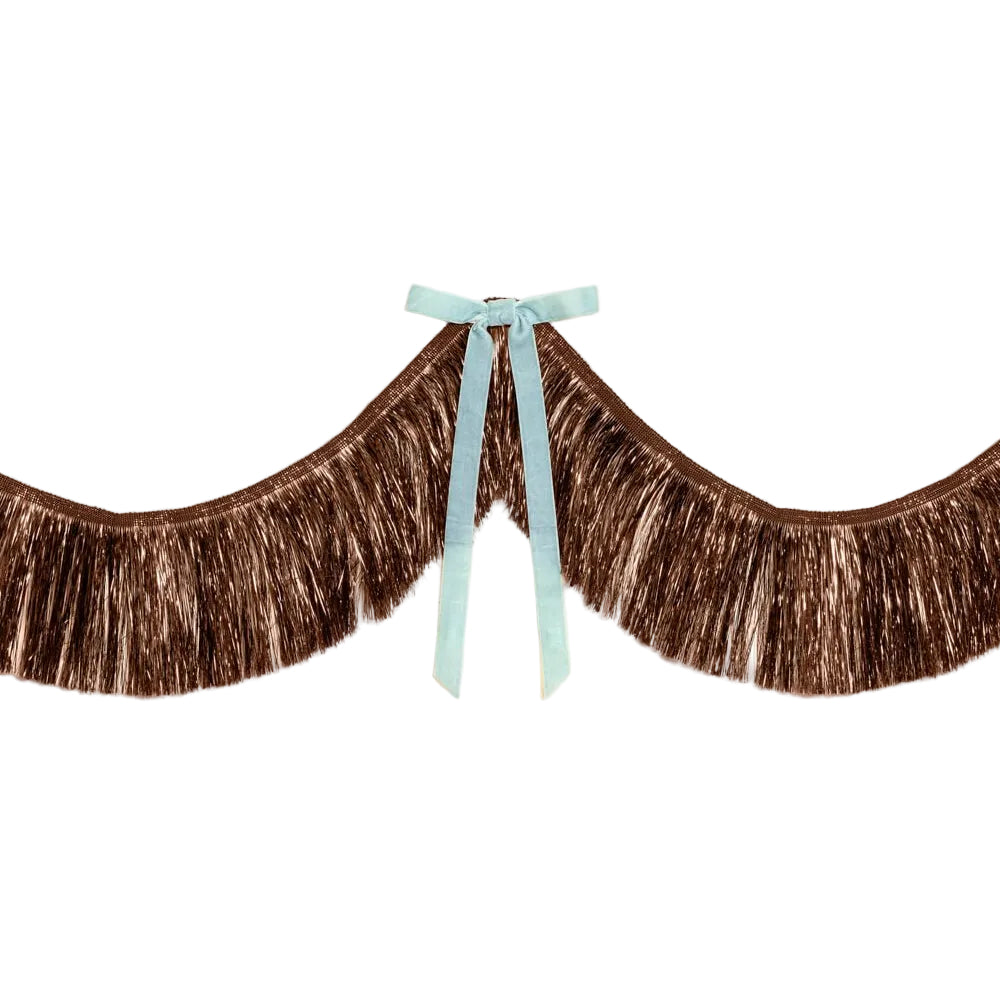 Brown metallic fringe backdrop with a light blue velvet bow at the center, hung against a pale beige wall