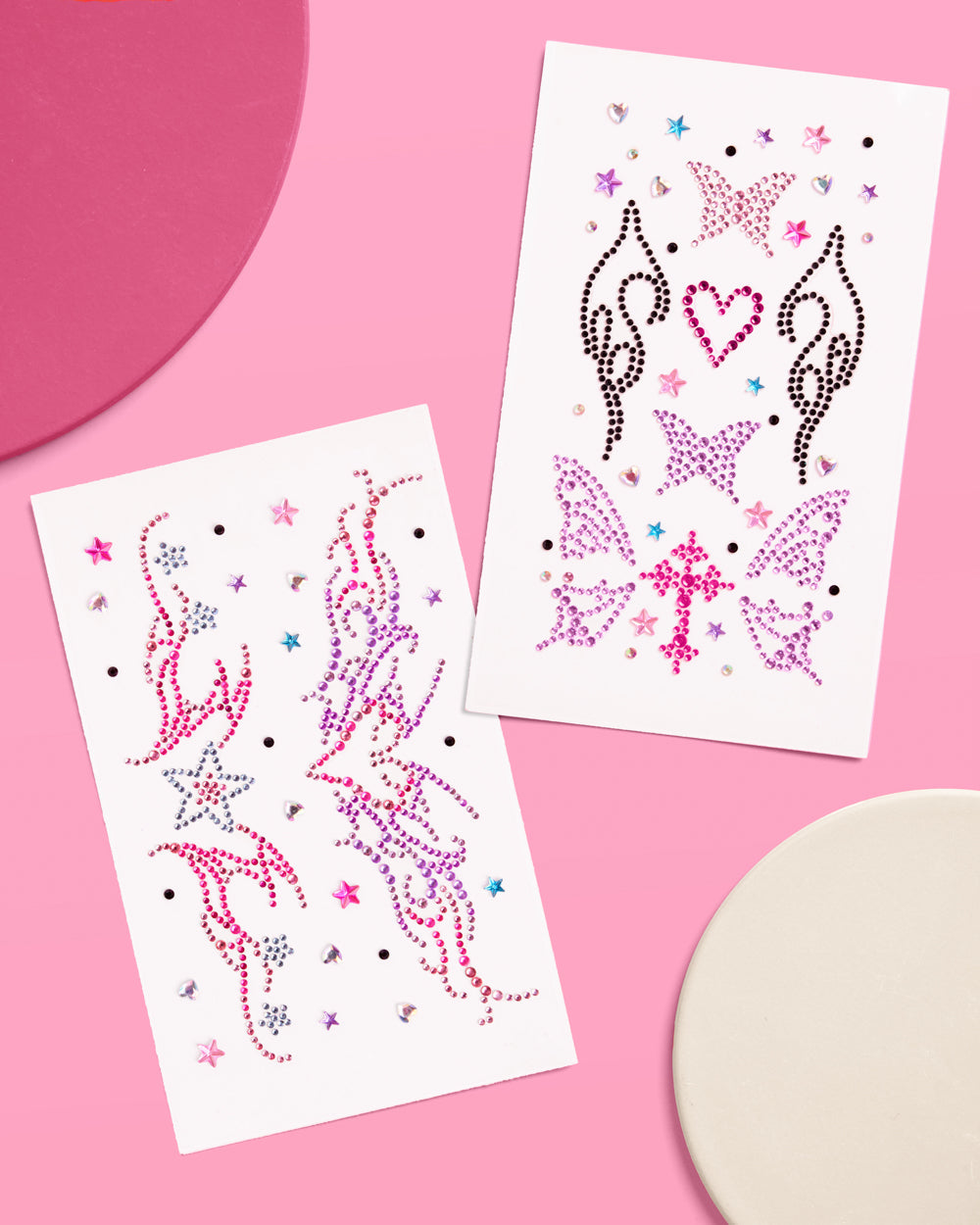Two sheets of self-adhesive Y2K body gems in pink, purple, black, and silver on a pink surface