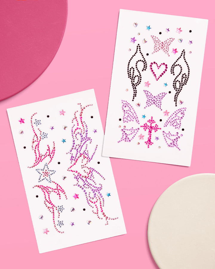 Two sheets of self-adhesive Y2K body gems in pink, purple, black, and silver on a pink surface