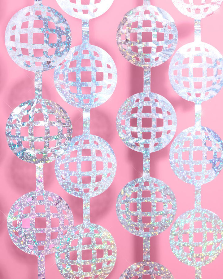 Layered silver disco ball cutouts on a curtain backdrop against a pink wall