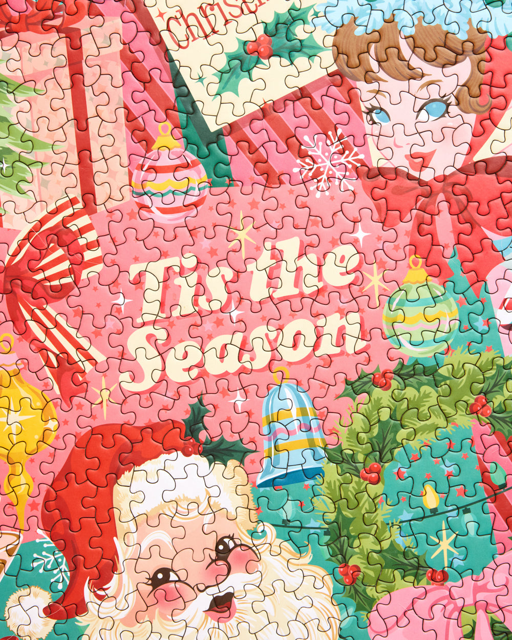 Close-up of Pinkmas puzzle pieces showing Santa, a wreath, ornaments, and the words Tis the Season.