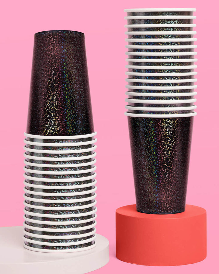 Two tall stacks of black iridescent paper party cups against a pink background