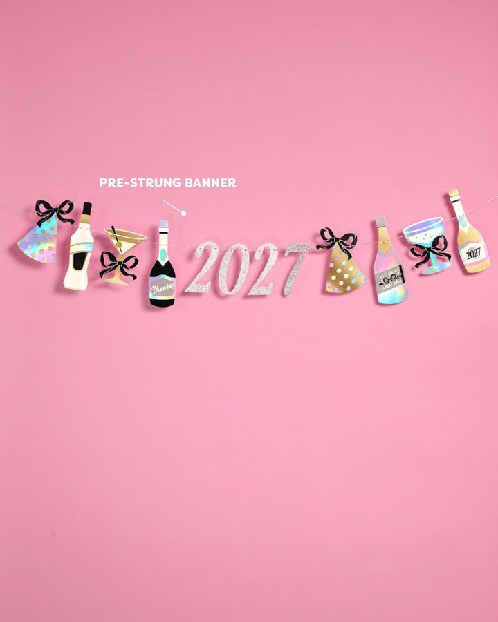 Pre-strung 2027 New Year banner with bottles, glasses, and party hats against a pink background.