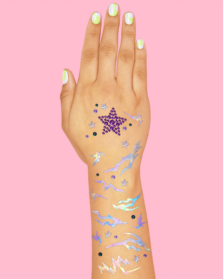 Hand and forearm decorated with purple star gems, small silver stars, and iridescent lightning stickers.