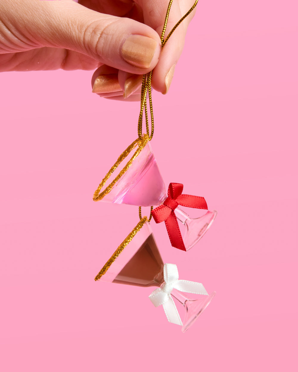 Hand holding a pink martini and an espresso martini ornament by gold string to show their small hanging size