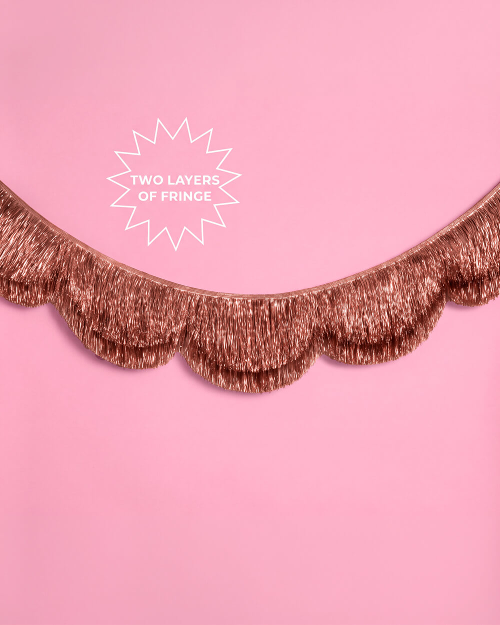 Rose gold scalloped fringe garland swagged across a pink wall with a Two Layers of Fringe callout