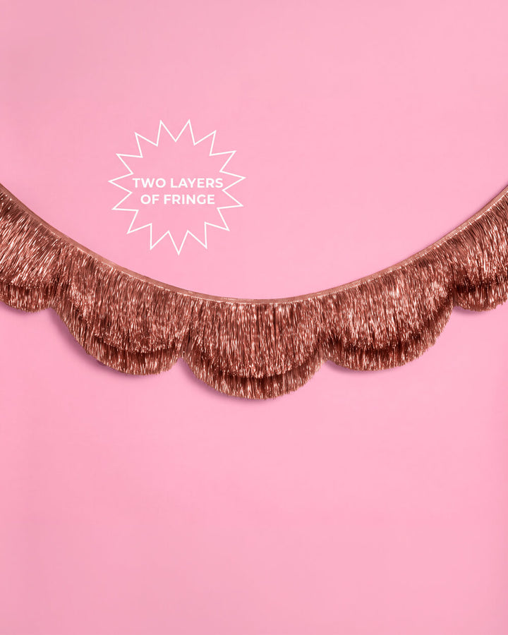 Rose gold scalloped fringe garland swagged across a pink wall with a Two Layers of Fringe callout
