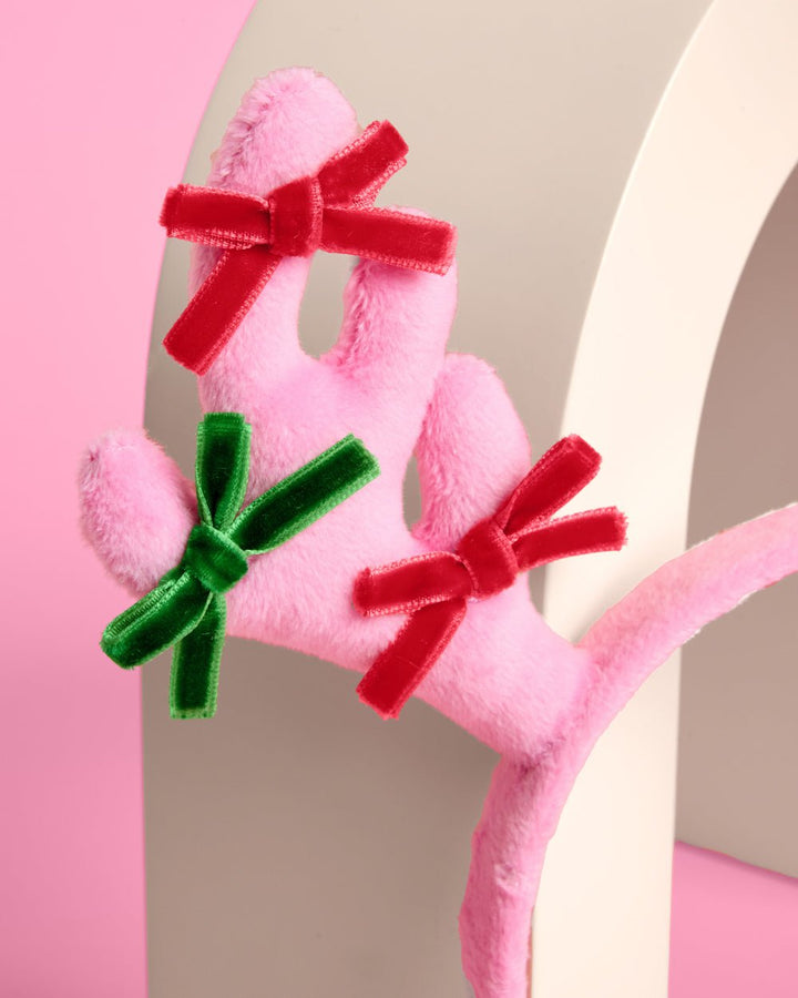 Close-up of a stuffed pink plush antler tied with red and green velvet bows