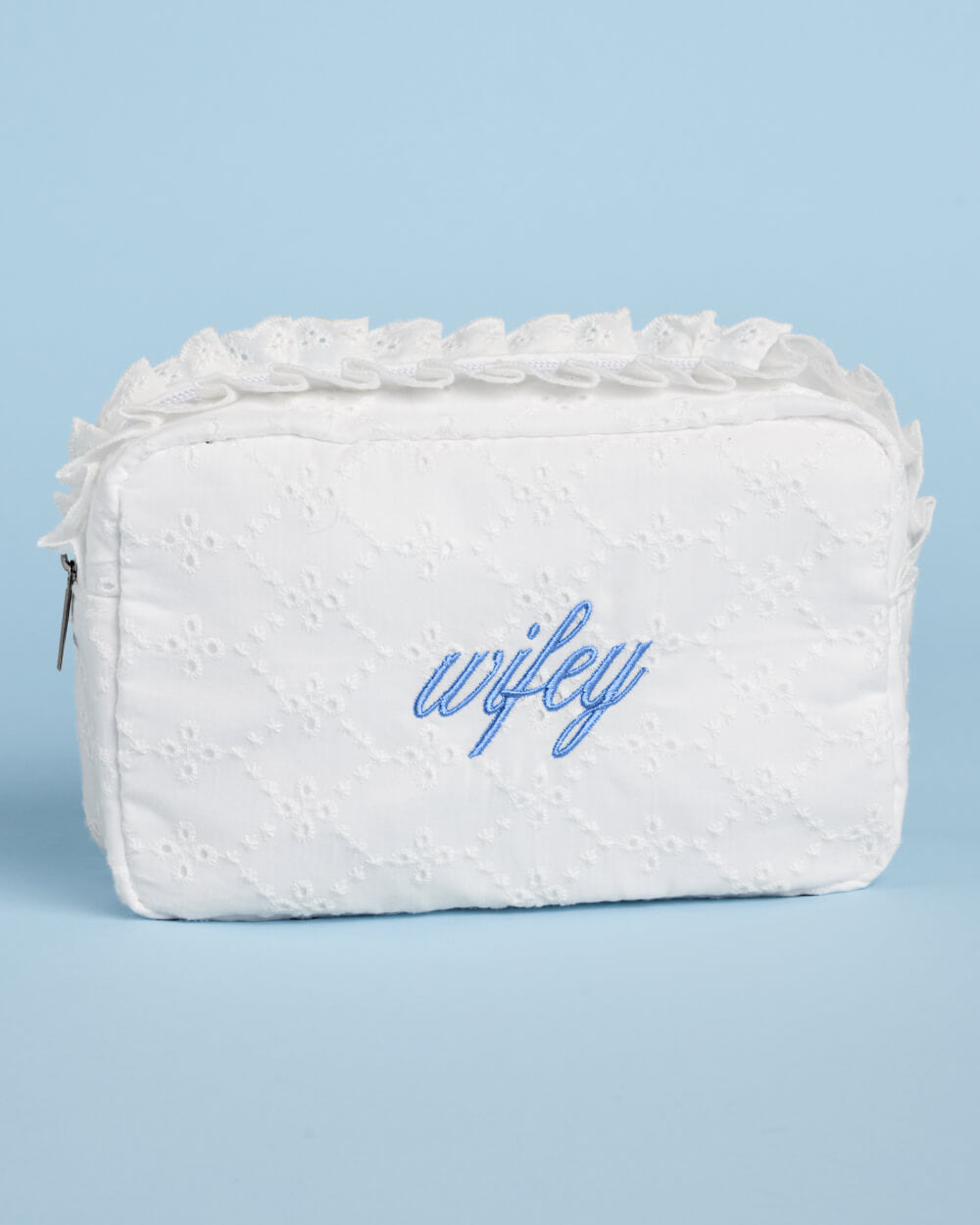 Front view of a white rectangular eyelet cosmetic bag with blue wifey lettering and ruffled top trim.