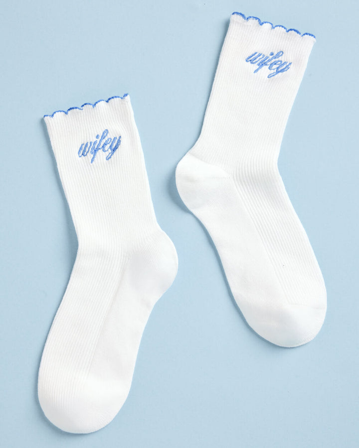 Pair of white wifey crew socks laid flat side by side on blue, a something blue gift for the bride
