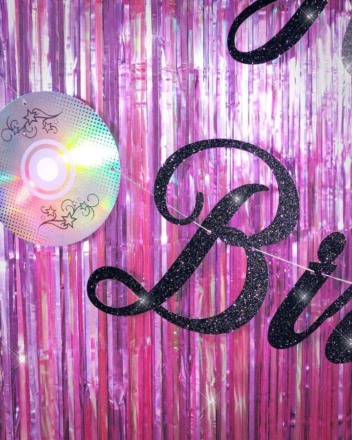 Close-up of black glitter Birthday lettering and an iridescent foil CD on the Y2K banner against purple fringe