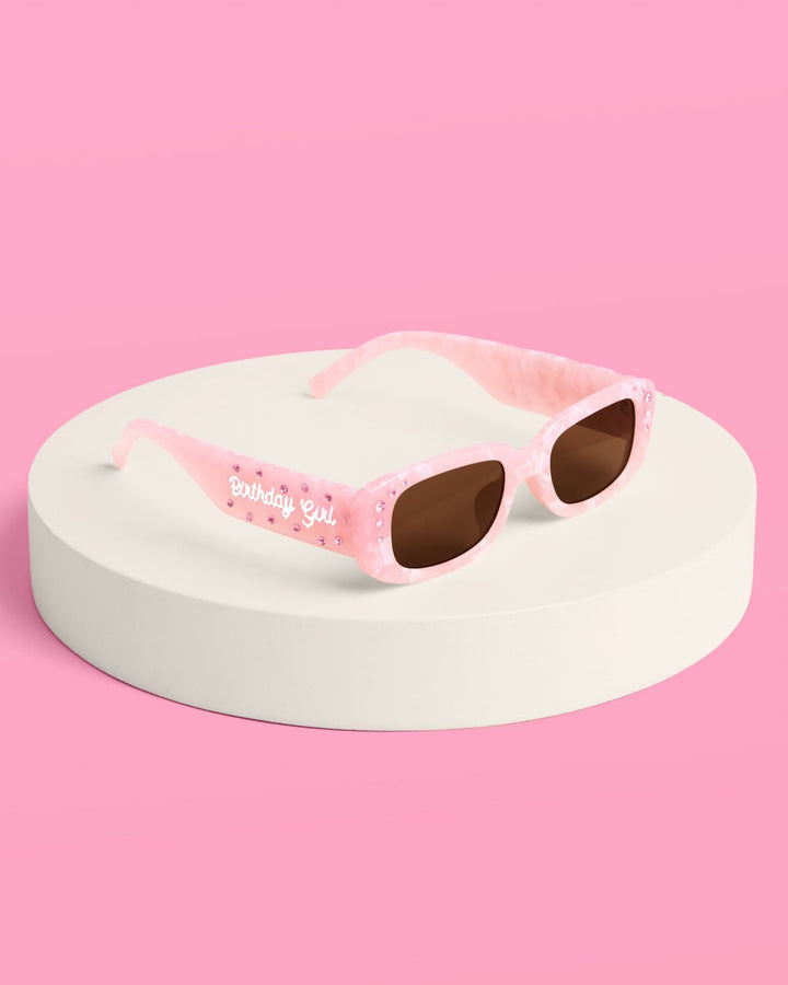 Pink marble Birthday Girl sunglasses displayed on a round white pedestal