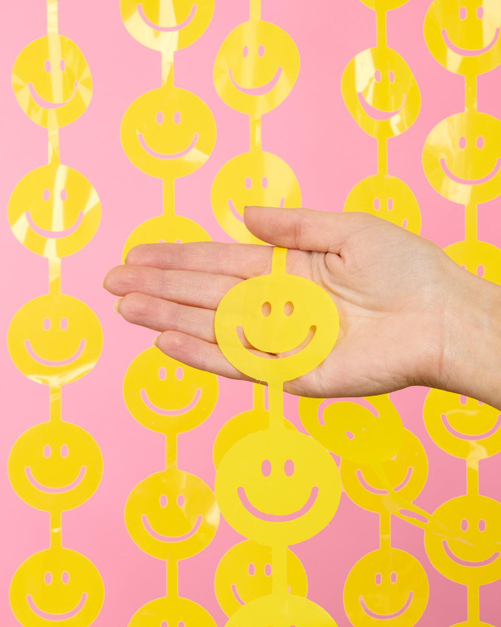Hand holding one yellow smiley face cutout to show its palm size against the curtain