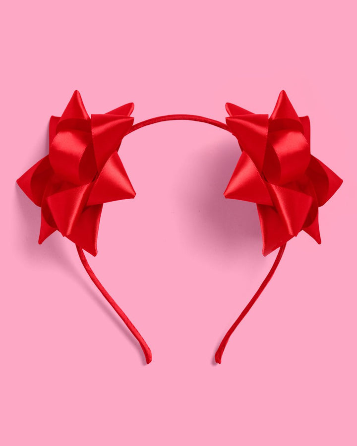 Red bow Christmas headband with two oversized satin gift bows on a slim red band, on a pink background
