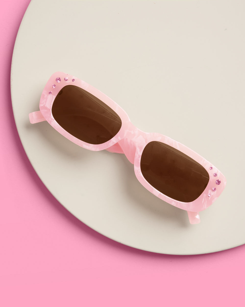 Pink marble birthday sunglasses with rhinestone corners on a cream circle