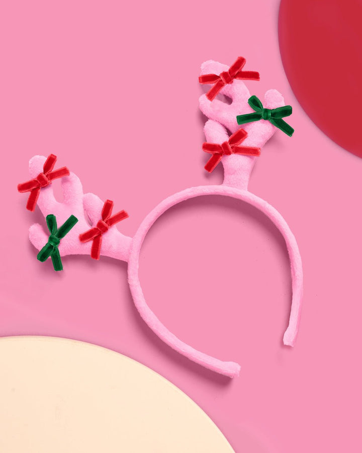 Angled view of the pink reindeer headband with bows on both antlers beside a red ornament