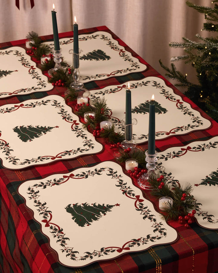Holiday table set with Christmas tree placemats, candles, and greenery