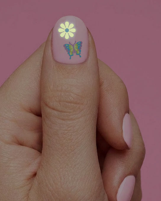 Thumb wearing a yellow daisy and a butterfly nail sticker from the groovy glow nail sticker set