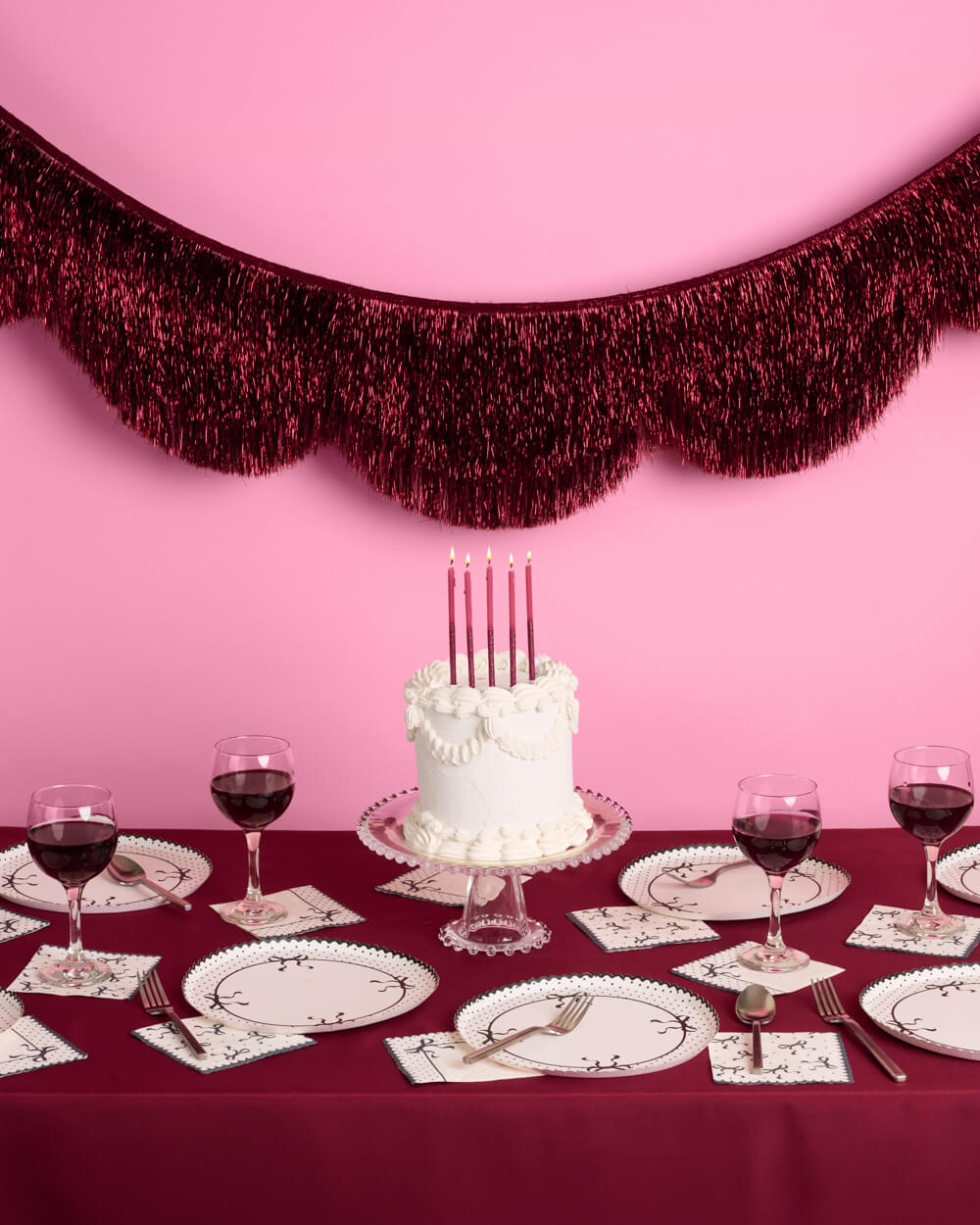 Burgundy scallop fringe banner hung above a birthday table with white cake, red wine, and burgundy linens