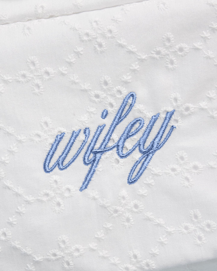 Close-up of blue script wifey embroidery on white floral eyelet cosmetic bag fabric.