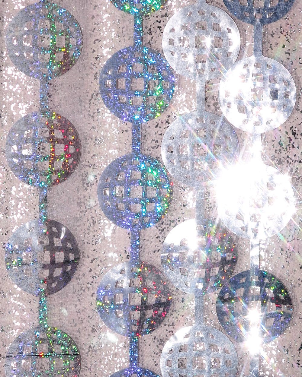 Silver disco ball curtain strands catching direct sunlight against a stone wall
