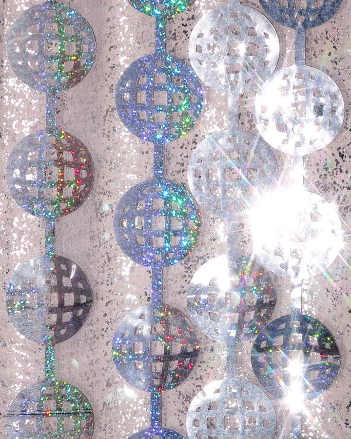 Silver disco ball curtain strands catching direct sunlight against a stone wall