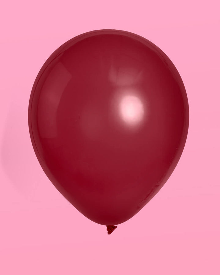 Single pomegranate burgundy latex balloon on a pink background