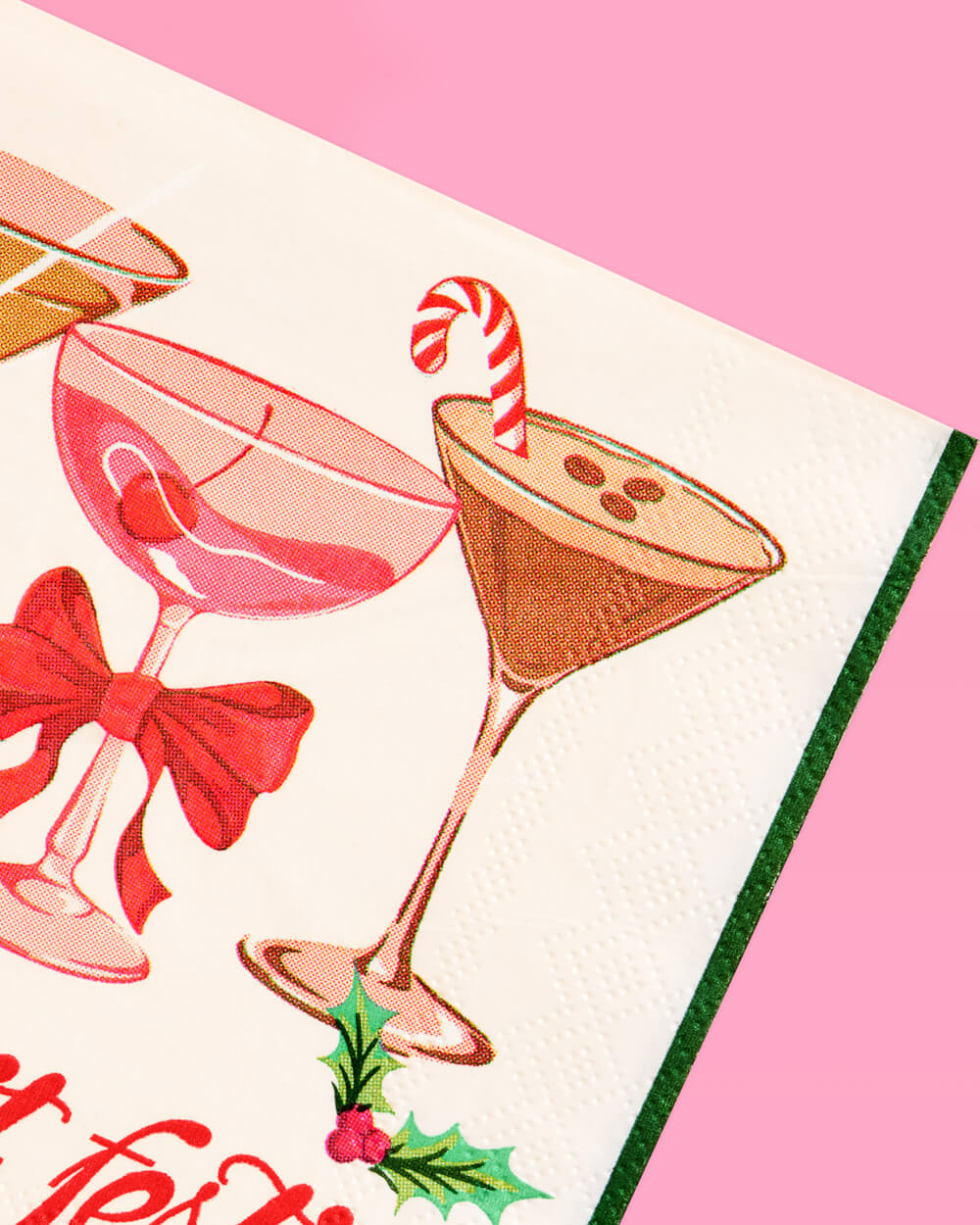 Close-up of an espresso martini with a candy cane and a pink cocktail with a red bow printed on a holiday napkin