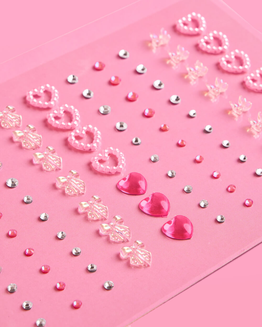 Decorative pink paper with heart and flower cutouts gems and small beads on a pink background