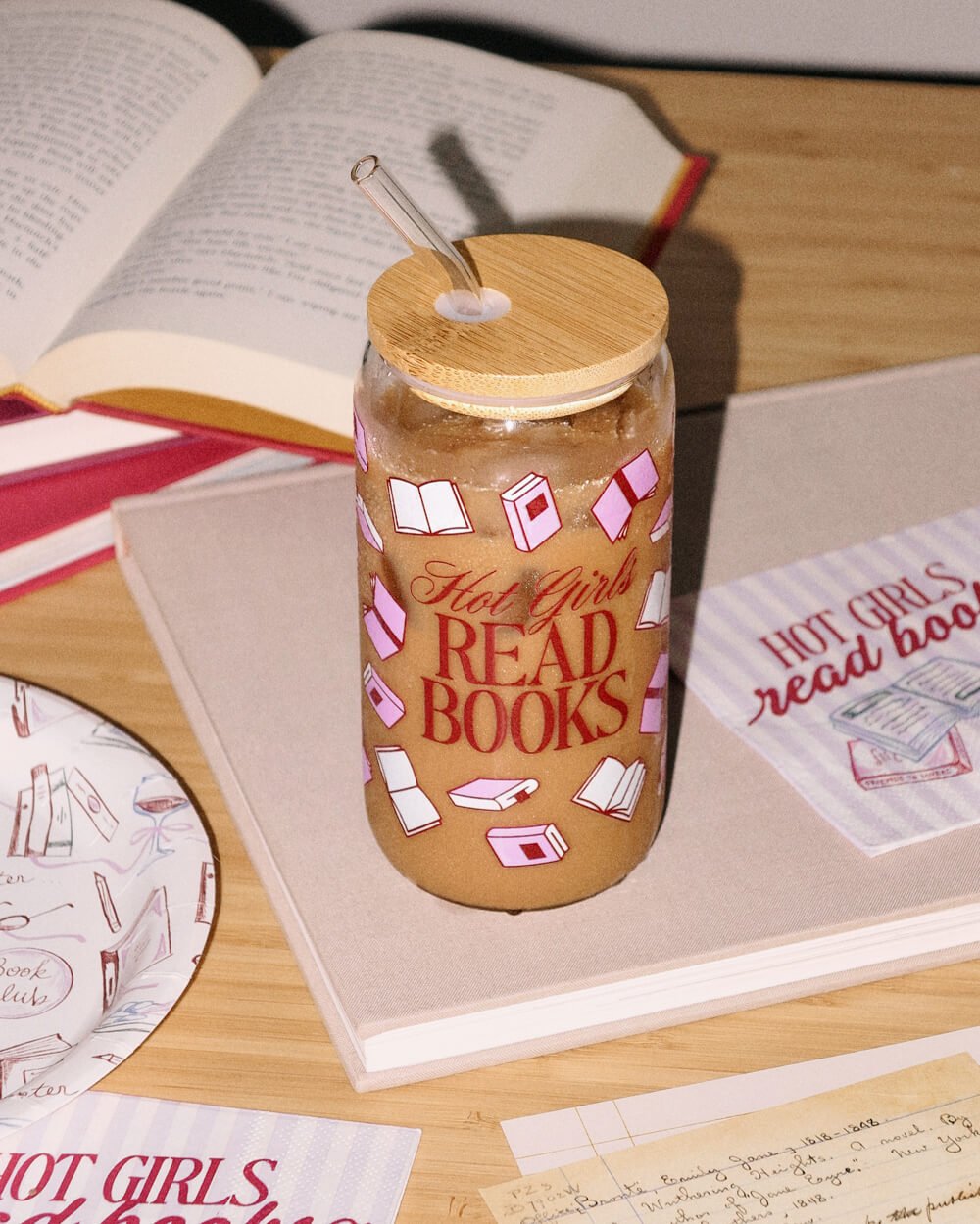 Book club tumbler with iced coffee on a reading table beside open books and Hot Girls book club napkins