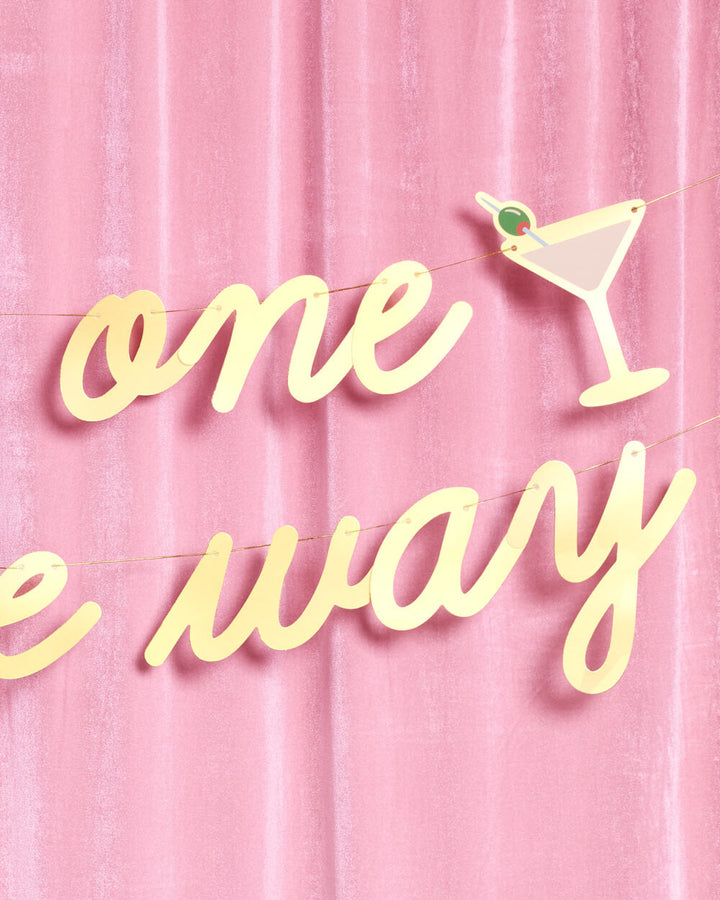 Detail of gold foil one on the way lettering and a martini glass icon with a green olive on a velvet curtain
