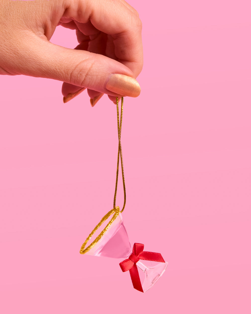 Pink martini ornament with a red bow and gold glitter rim dangling from gold string held between two fingers