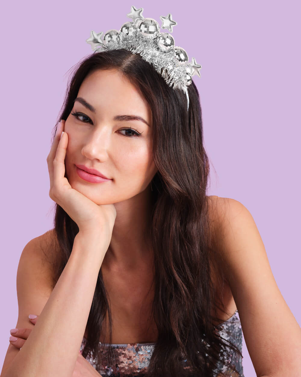 Woman resting her chin on her hand while wearing the silver disco ball and star headband on lilac
