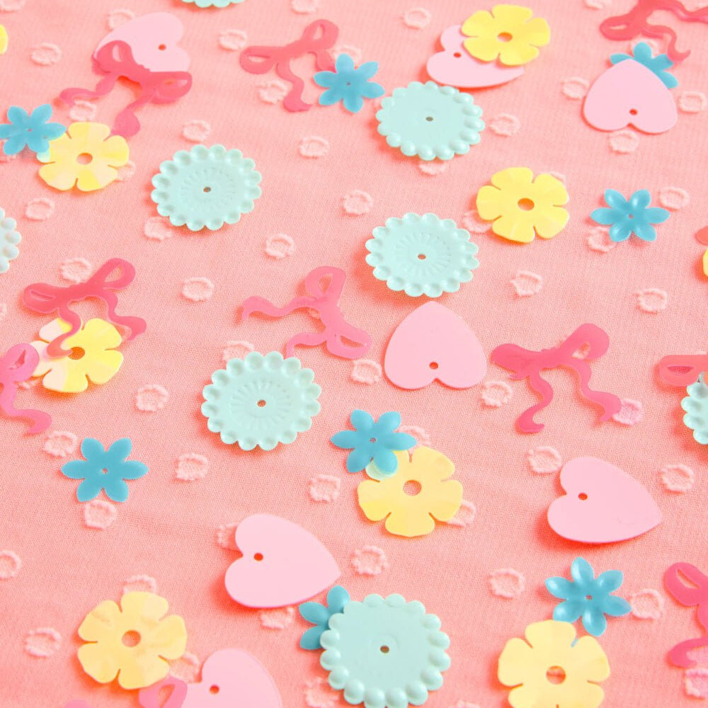 Pastel plastic confetti in teal, pink, and yellow shown at half-inch scale on pink