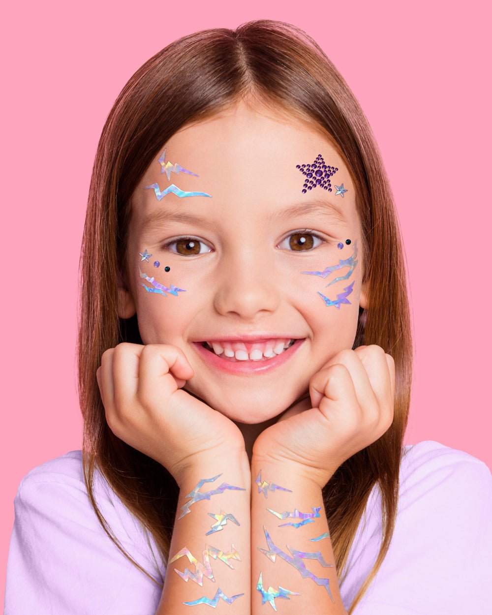 Child wearing purple star and iridescent lightning face gems, with matching stickers on both wrists.