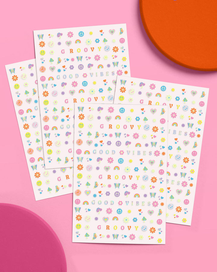 Four sheets of groovy glow in the dark nail art stickers fanned out on a pink and orange background