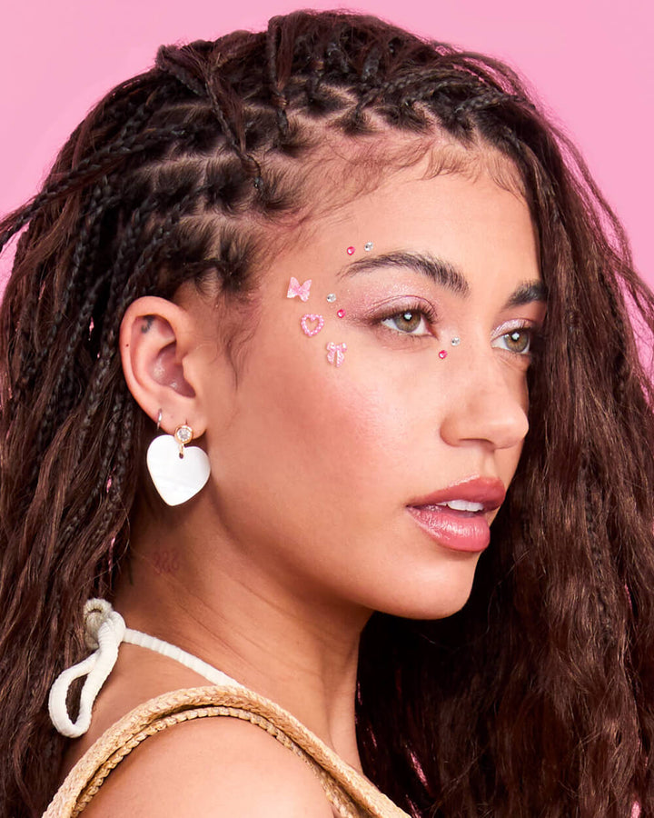Woman with braided hair and pink background wearing face gems