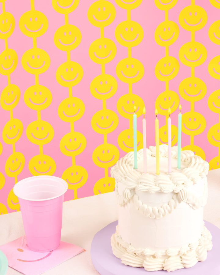 Yellow smiley face foil curtain strands hanging against a soft pink wall
