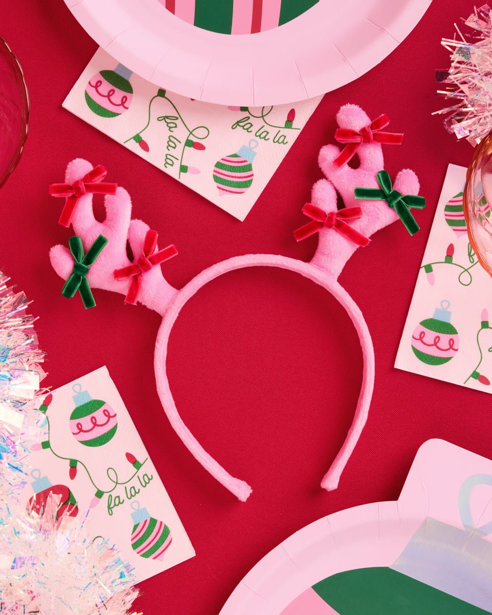 Pink reindeer antler headband on red with holiday napkins and pink plates for a Christmas party
