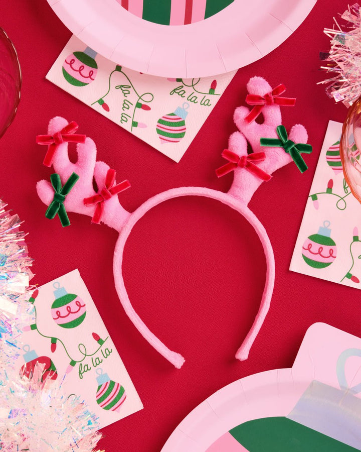 Pink reindeer antler headband on red with holiday napkins and pink plates for a Christmas party