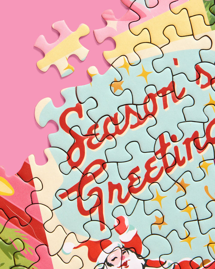 Close-up of interlocking Pinkmas puzzle pieces with red Seasons Greetings lettering and yellow stars.
