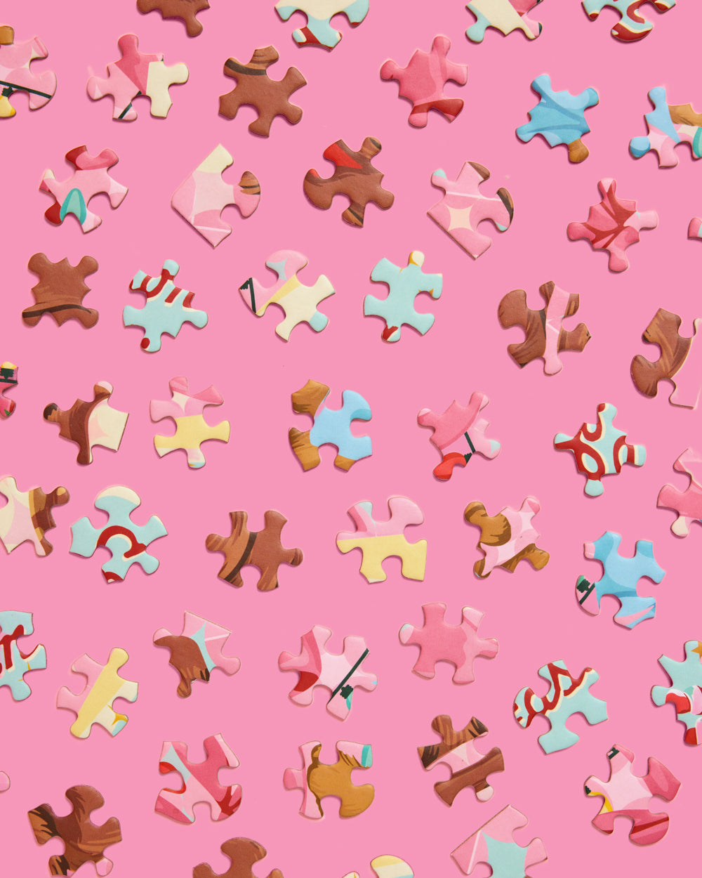 Loose multicolored Pinkmas jigsaw puzzle pieces scattered across a pink background.