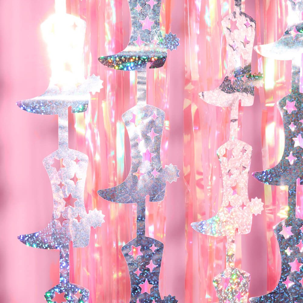 Close-up of silver and pink holographic cowboy boot cutouts with stars on a pink fringe backdrop