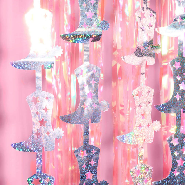 Close-up of silver and pink holographic cowboy boot cutouts with stars on a pink fringe backdrop