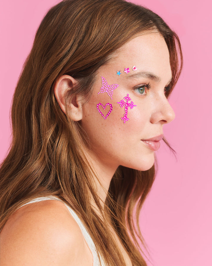 Pink Y2K face gems with a heart and a cross placed on the cheekbone of a smiling woman