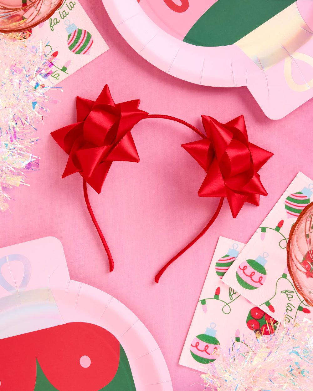 Red satin bow headband styled with pink Christmas plates and tinsel for a holiday party table