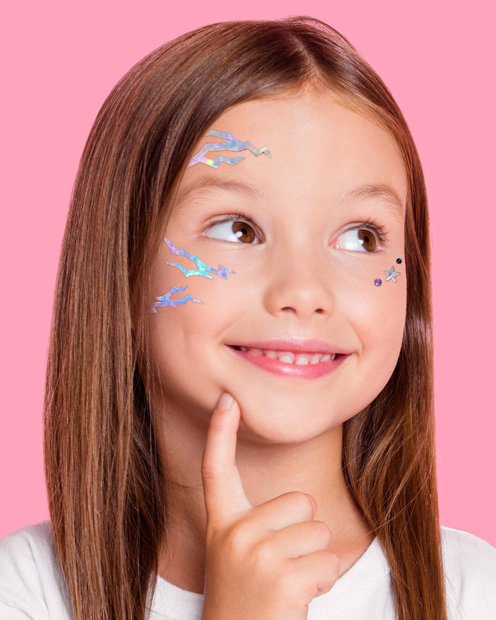 Child modeling iridescent lightning stickers and small star and round gems on the forehead and cheeks.