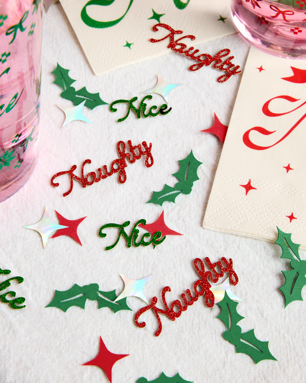 Naughty or Nice Christmas confetti spread out to show the words, holly leaves, and stars
