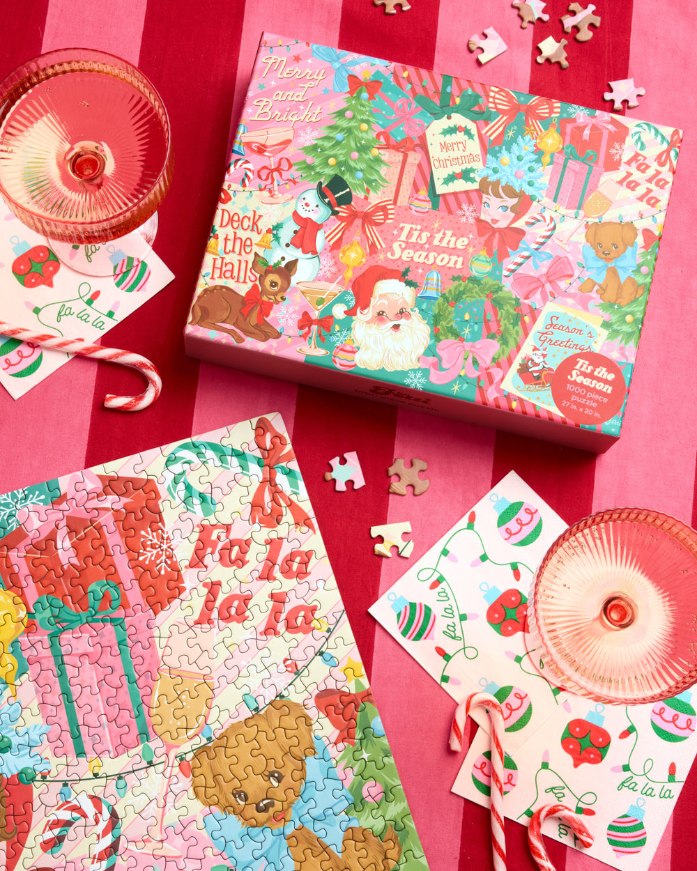Pinkmas puzzle box and assembled Christmas puzzle styled with pink glasses and candy canes on a striped table.